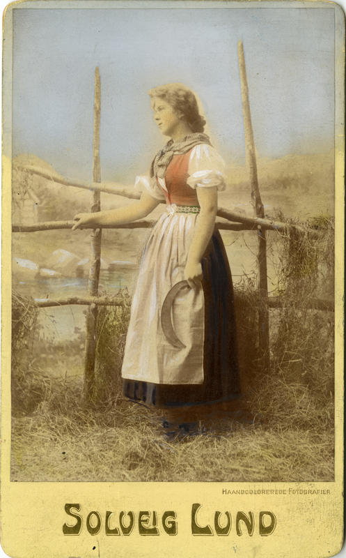Kolorert studiofotografi av kvinne med sigd og høyhesje. 1906. (Foto/Photo)