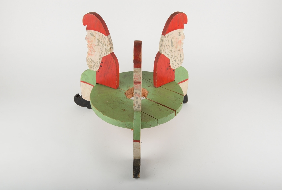 Juletrefot utskåret i tre, med 3 nisser som sitter rundt sirkelen hvor juletreet festes. Nissenes bein fungerer som gulvstøtter/føtter.

Den runde platen er malt grønn. Julenissene er dekorert med rødmalt lue, hvitt skjegg, rød jakke, grønne bukser med rød kant langs kneet, hvite knestrømper og svarte sko.