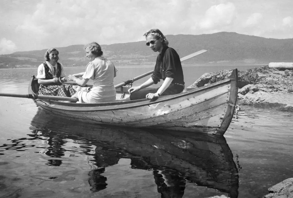 Robåt (dreggebåt, mjøsbåt, Hollandbåt), Til høyre sitter Lumi Johannessen, damen i midten er Ruth Oline Engebretsen, født Carlsen, født i 1915. Hun var nabo til Lumi, siste er ukjent. Her sittende i båten utenfor "Lia, " hytta til baker Johs. Johannessen på Jessnes i Furnes. Mjøsa. Båten er ikke malt (ant. lakkert), har utliggere for årene, typiske for mange av mjøsbåtene.