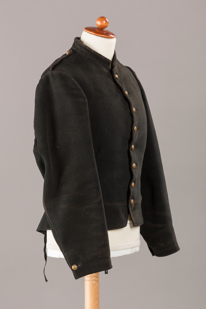 Form: Enkeltspent.

Foret med lin. Forsterket med silke på et lite stykke på ryggen. 12 messingknapper med mønster og tallet 1. Hempe i lin. Bendelbånd med knappehull.