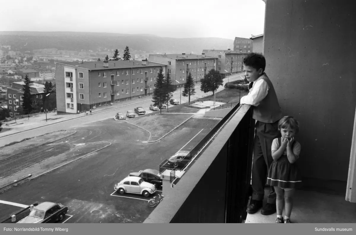 Nya flerfamiljshus vid Ludvigsbergsvägen 12-20. Exteriörbiuld samt från balkongen och köket hos en familj. Två barn på balkongen och en kvinna i köket.