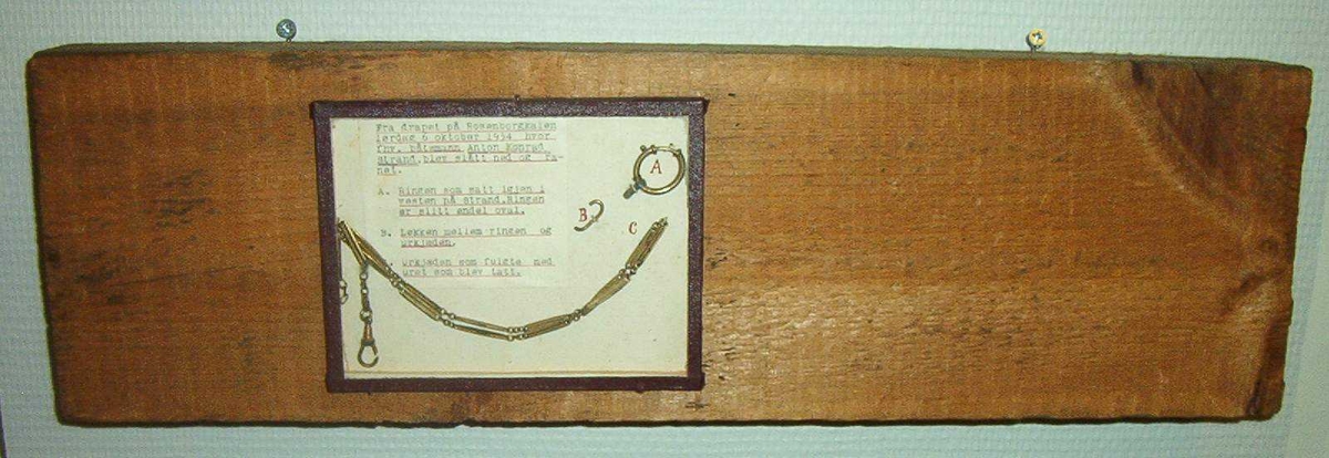 Trestokk brukt som drapsvåpen. Ring og urkjede, gullfaget opprinnelig montert på en treplate med tekst.