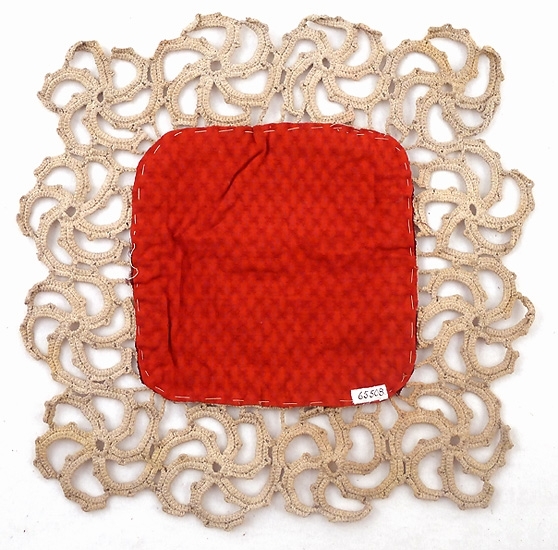 Rödbrun fyrkant av sammet i mitten, på baksidan starkt rött ylletyg med små mönster, runt omkring bred virkad kant av stora virvelformade mönster.