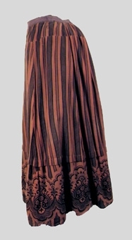 Ljus brunaktigt röd kjol med tryckt mönster i svart. Modellen består av fem kilformade våder vilka är sammanfogade med maskinsöm. Kjolen är rynkad mot linningen mitt bak. Ett veck, ca 3 cm brett, är sytt runt kjolens nedre del. Kjolen är skodd nedtill med ett blåaktigt rött bomullstyg, monterat med kastsöm. Ett svart sammetstyg är fäst mot kjolens nedre kant. Sprund mitt bak, vilket knäpps med en hake fäst i linningen. Hängband är monterade i sidorna mot linningens avigsida. Kjolens tyg är ruggat på avigsidan.