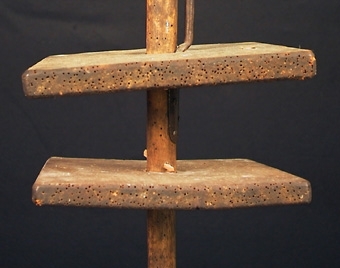 Enl liggare:
"Ljuskärring (?) Trästång med rund fot, två träskivor trädda på stången och mellan dessa en svarvad träskål. På övre delen av stången fem klämmor av järn, möjligen till att fästa trästickor i. En smal järnten utmed övre hälften - okänd användning H 114 cm, br 25 cm. Defekt."