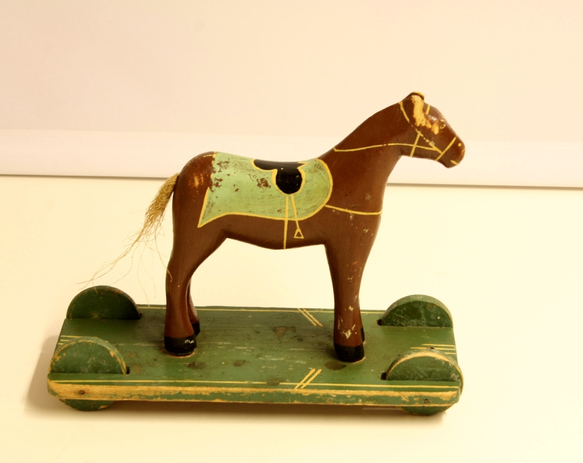 Form: Hestefigur montert på ei rektangulær plate med fire hjul av tre.