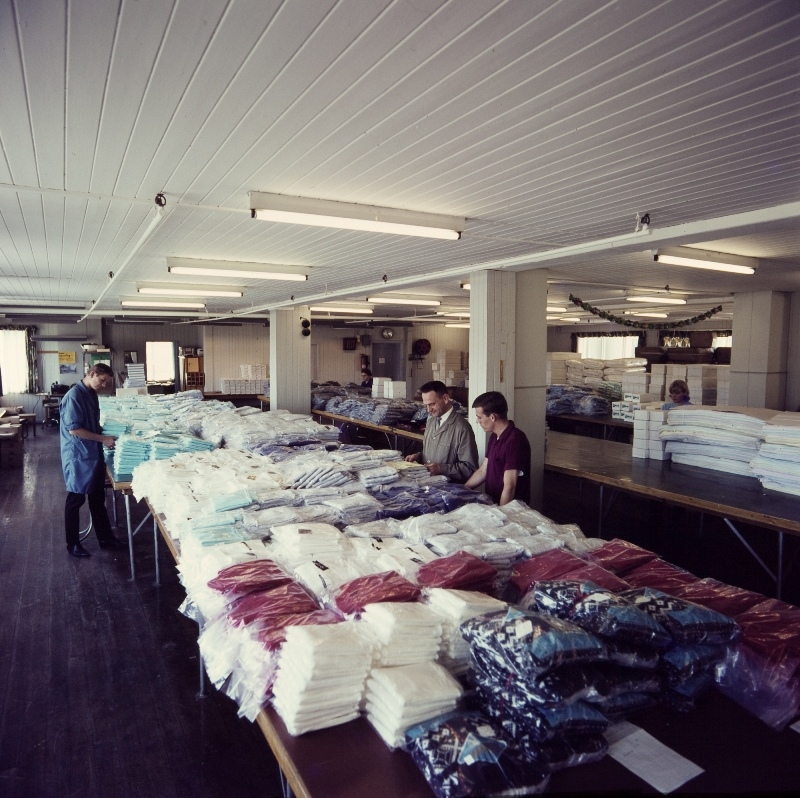 Tre arbeidere står ved en pakkedisk i manufaktur-engros-lageret til Jonas Øglænd Sandnes.
