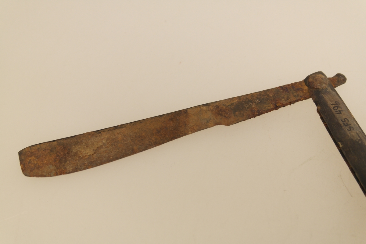 Barberkniv (A) med futeral (B). 
A) Barberkniv med skaft i bein og blad i støpt stål. Bladet kan foldes inn i skaftet.
B) Futeral i svart papp. Innpreget harlekinmønster på den ene siden, og bladranker (?) på den andre siden.
Innpreging i bladet.