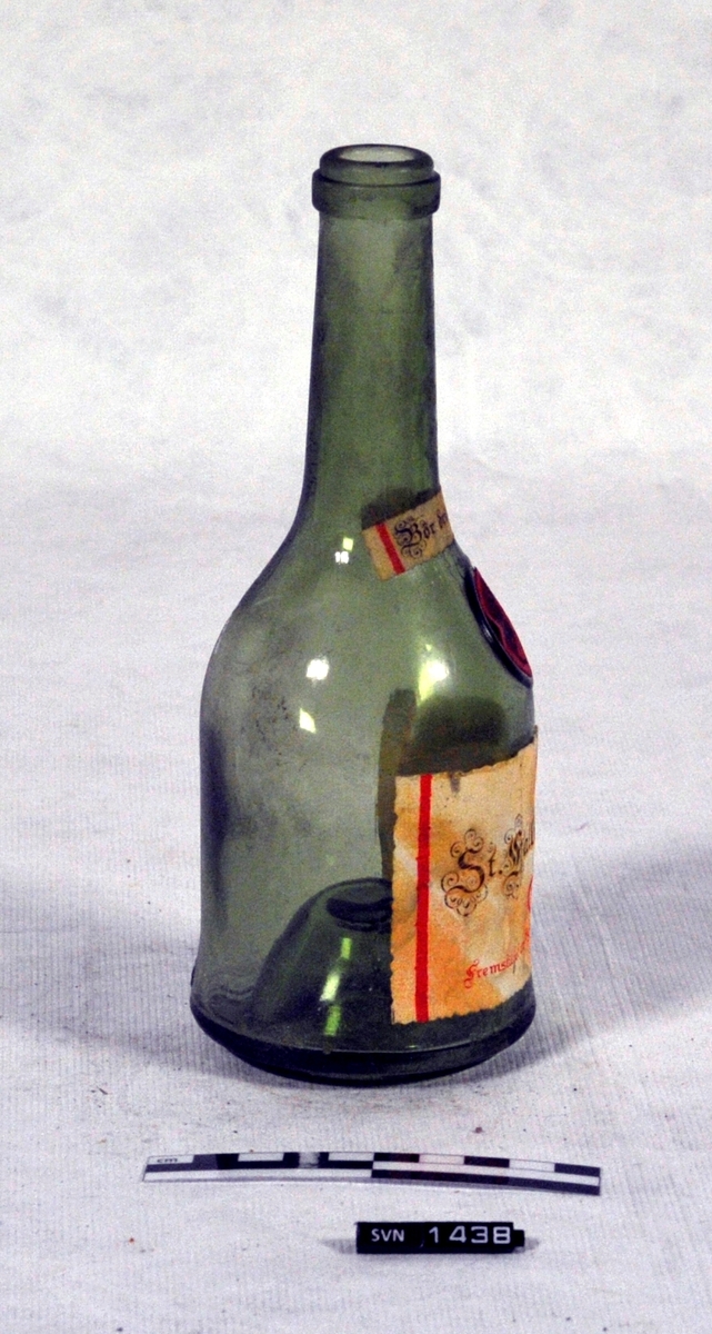 Grønn flaske med lang hals.
Flasken er uten innhold og har ikke kork.
Flasken har to etiketter og en voksmerke.