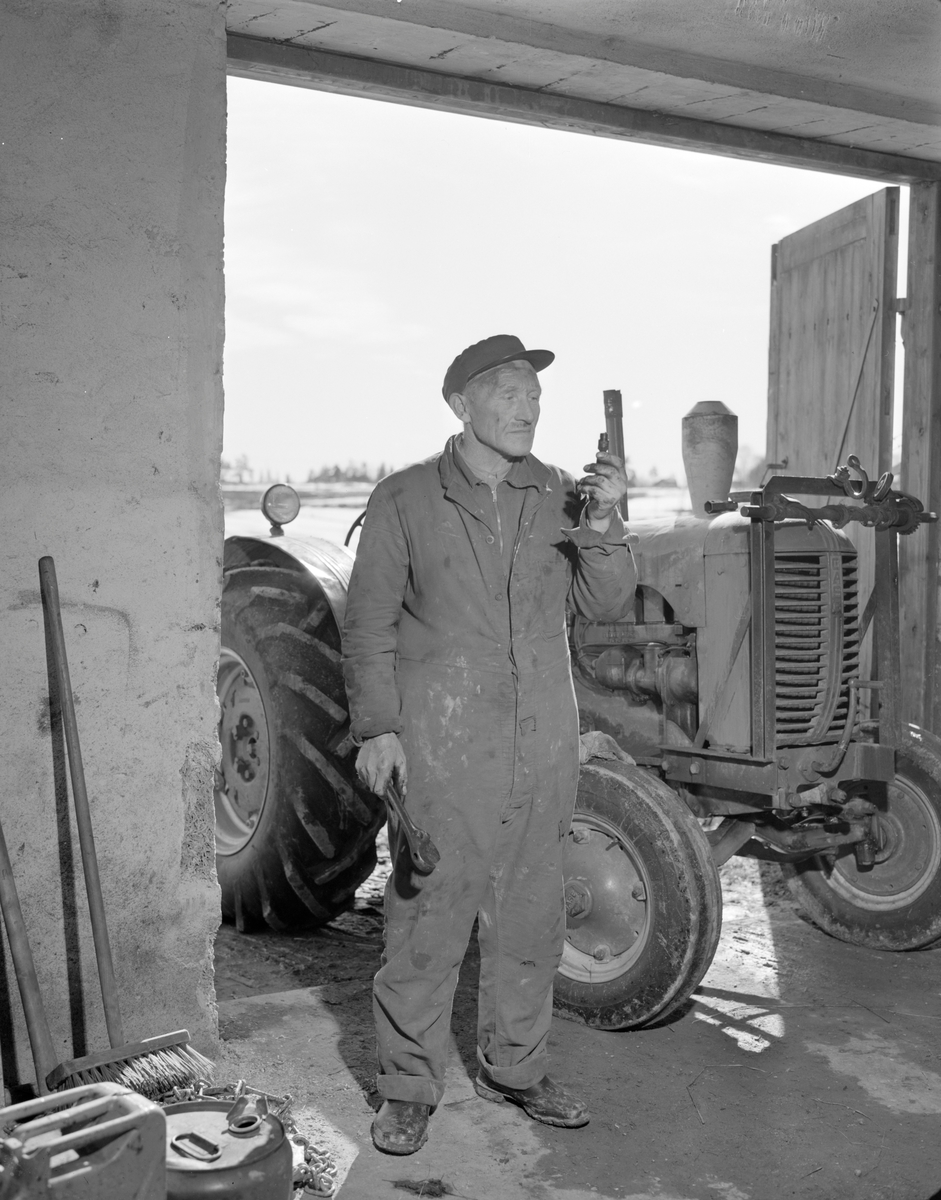 Norsk landbruks jubileumsutstilling 1959. Gårdsarbeider og traktor, i døren inn til et verksted.