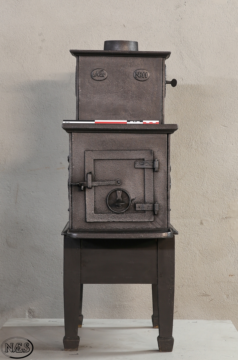 Kokeovn med to muser på enkel profillist. En fløytespillende og en dansende. Begge med draperier. Kokeanretning i topplaten til 1.etg. Ovnsdør på kortside. Rosett på begge sideplatene 2.etg. Den ene er løs og fungerer som ventil. Innskrift på frontplate og bakplate 2.etg. Røykuttak i toppen.