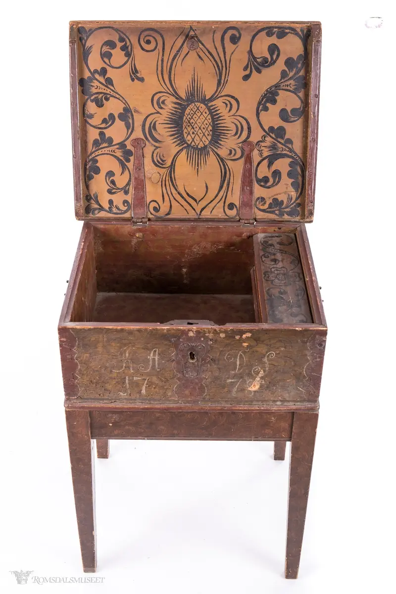 Ensfargede, bølgede dekorfelter midt på og på sidene av lokket, likeså rundt nøkkelhull og ved hjørnene.