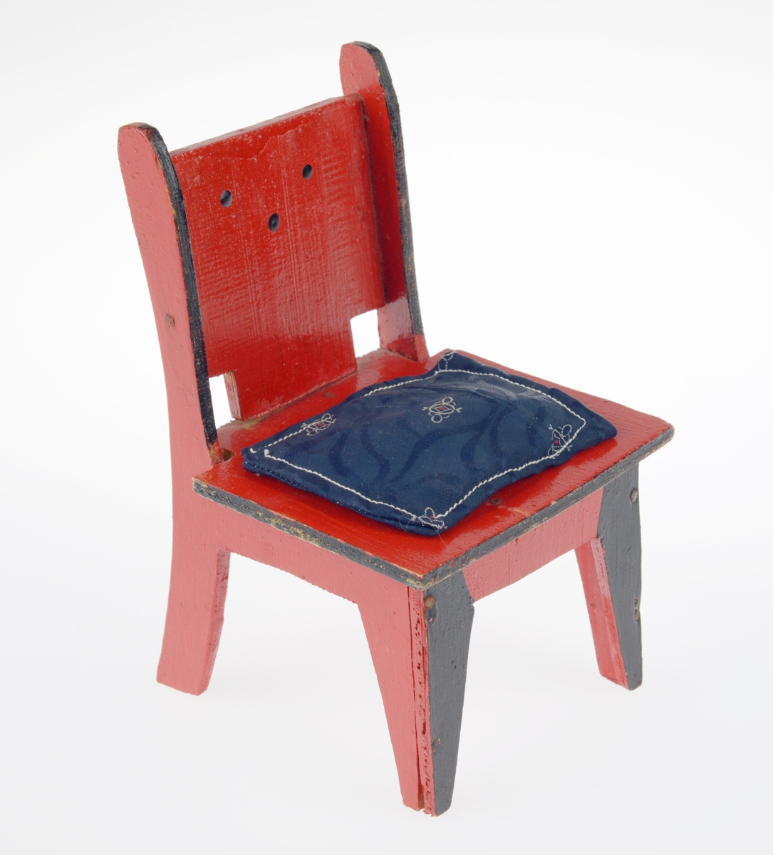 Et dukkemøblement bestående av bord (FTT.54416.01), en benk med pute (FTT.54416.02) og to stoler med puter (FTT.54416.03 og FTT.54416.04). Alle møblene er laget av kryssfiner. Bordet er firkantet og er malt rødt med en svart stripe langs kanten. Benken er også firkantet. Armlenene er avrundet og noe kortere enn setet. I ryggen er det skjært ut tre firkanter. Benken er rødmalt med svarte kanter. Fronten på beina er også svartmalt. I ryggen er det malt seks prikker som utgjør to trekanter. Til benken hører det til en pute sydd av ullstoff. Den er dekorert med broderi, antageligvis gjort av et barn. Stolene er også firkantete. I ryggen er det skjært ut to firkanter. Stolene er rødmalte med svarte kanter, og fronten på stolbeina er også svartmalt. I ryggen er det malt tre prikker som utgjør en trekant. Til den ene stolen hører det til en pute sydd av ullstoff. den er dekorert med en brodert sommerfugl. Til den andre stolen er det en pute sydd av kunstig silkestoff. Ullputene er hvite med rød dekor. Den siste puten et blå med mønster i hvitt og rødt.