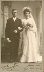 Brudepar, Bruden i hvit tilknappet kjole med slør og brudebu