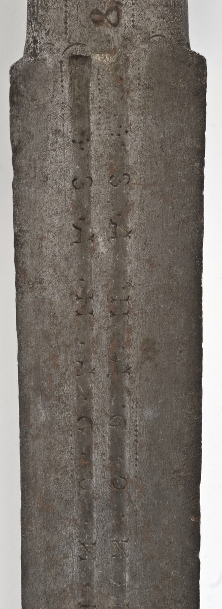 Rund pæreformet knapp med 10 fasetter  Tregrep. Flate svakt opp og nedbøyde  parerstenger med som ender i to fliker. Punslet dekor på parerstengene.
Asymetrisk kurvfeste med nyreformet parerplate på innsiden Prereplaten på utsiden er borte. Sidebøyler og håmdbøyle er formet av flate bånd. Skade på bånd på utsiden.
Tveegget rett klinge med  ovaklt  tverrsnitt  og to korte blodrender. Klingen har innskripsjon "SAHGON"