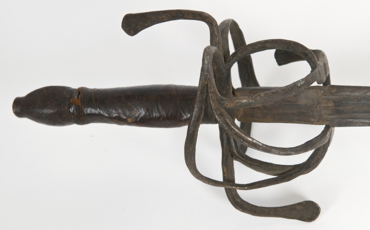 Plommeformet knapp. Tregrep  med lær bevokling.. Asymmetrisk feste med flate parerbøyler.  S formede parerstenger med utsmidde avslutninger..
Tveegget, rett klinge med rombeformet tverrsnitt og bred blodrand på begge siser 2 smale blodrender mot klingebrystet. Blodranden er merket WEILM KLEIN på begge sider. Klingen eravkortet.