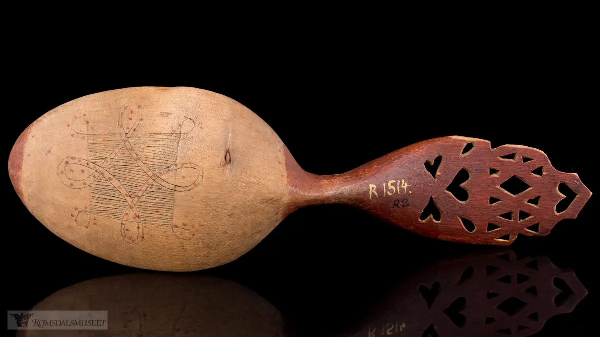 Skaftet perforert,-hjertering, selve skjeen abstrakt flate- og liljemønster med røde prikker.