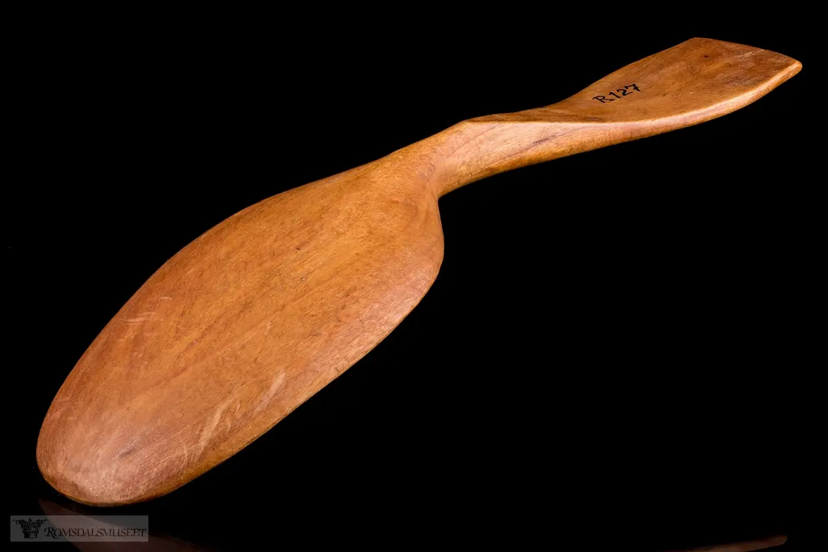 Enkelt formet og lakkert treskje uten dekor. Bredt flatt skaft og langt ovalt skjeblad.