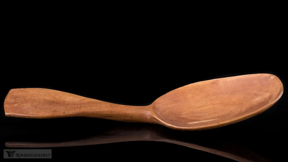 Enkelt formet og lakkert treskje uten dekor. Bredt flatt skaft og langt ovalt skjeblad.