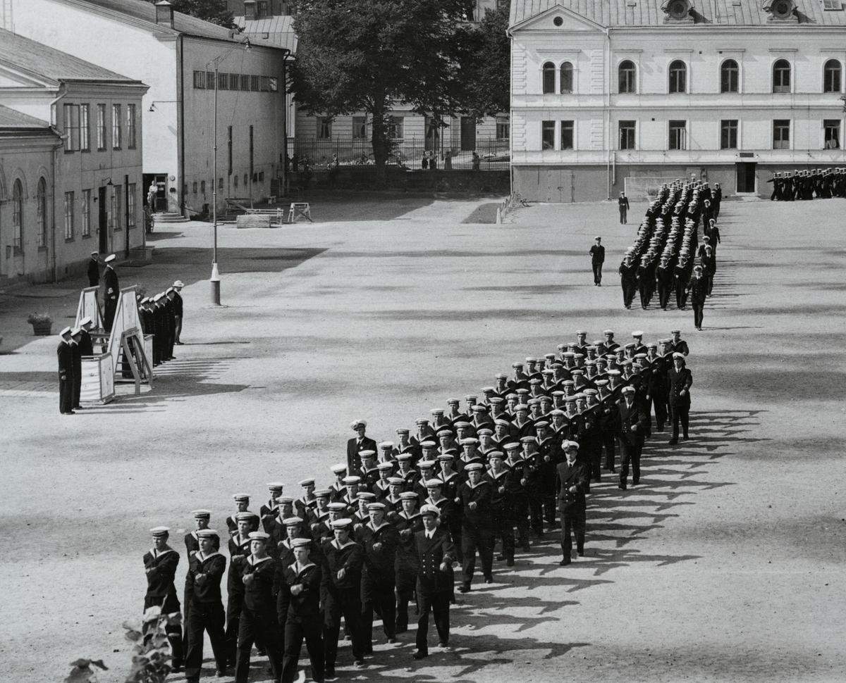 Uniformsklädda flottister marscherar över Sparre kaserngård. I bakgrunden syns bataljon Sparres kanslibyggnad uppförd omkring 1818.