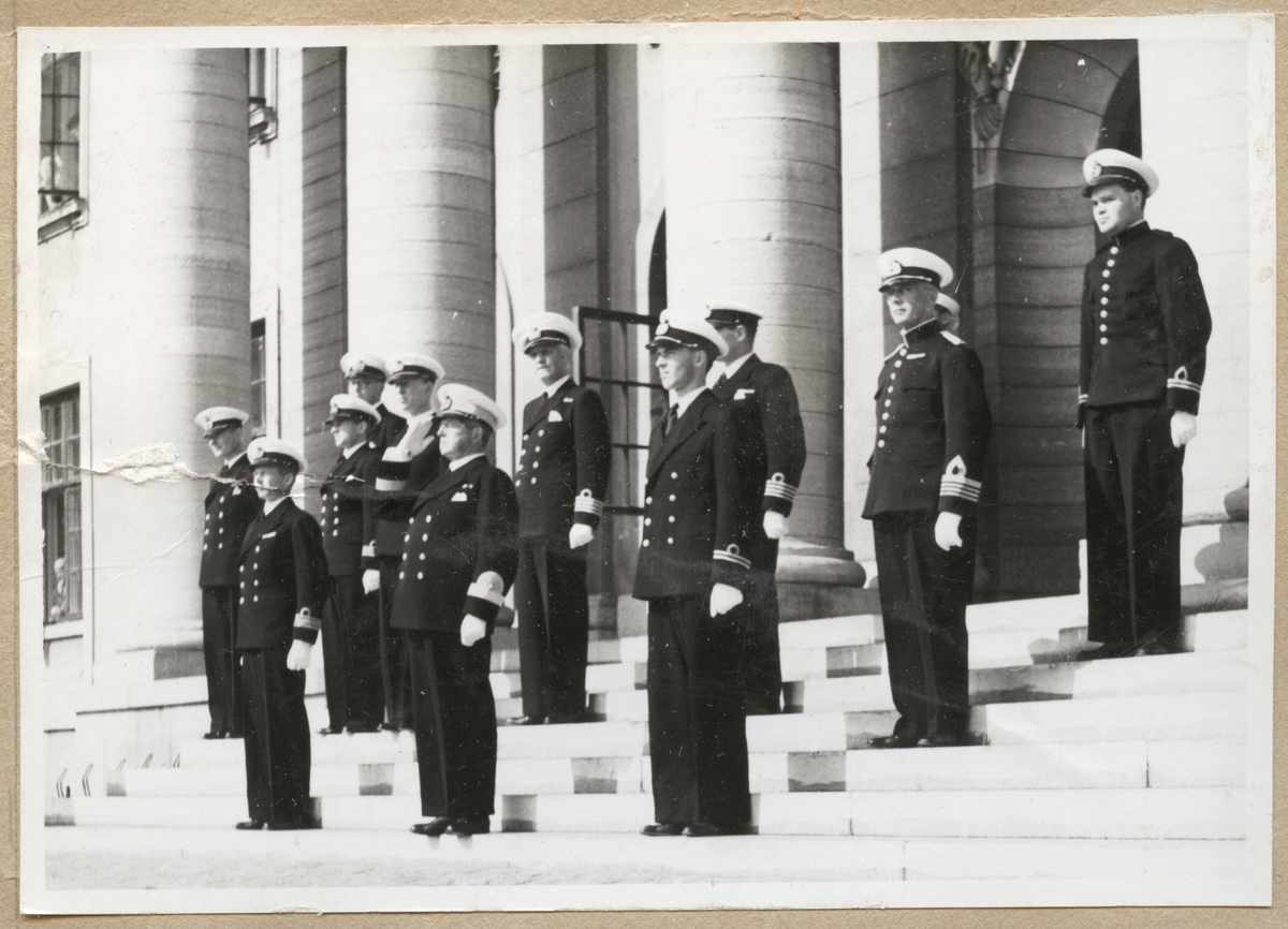 Uniformsklädda militärer av hög rang från marinen och amfibekåren står på trappan till Karlskrona rådhus. Bland annat syns kommendörer, kommendörkaptener och löjtnanter. I mitten i den främre raden står konteramiral Ehrensvärd och gör honör.