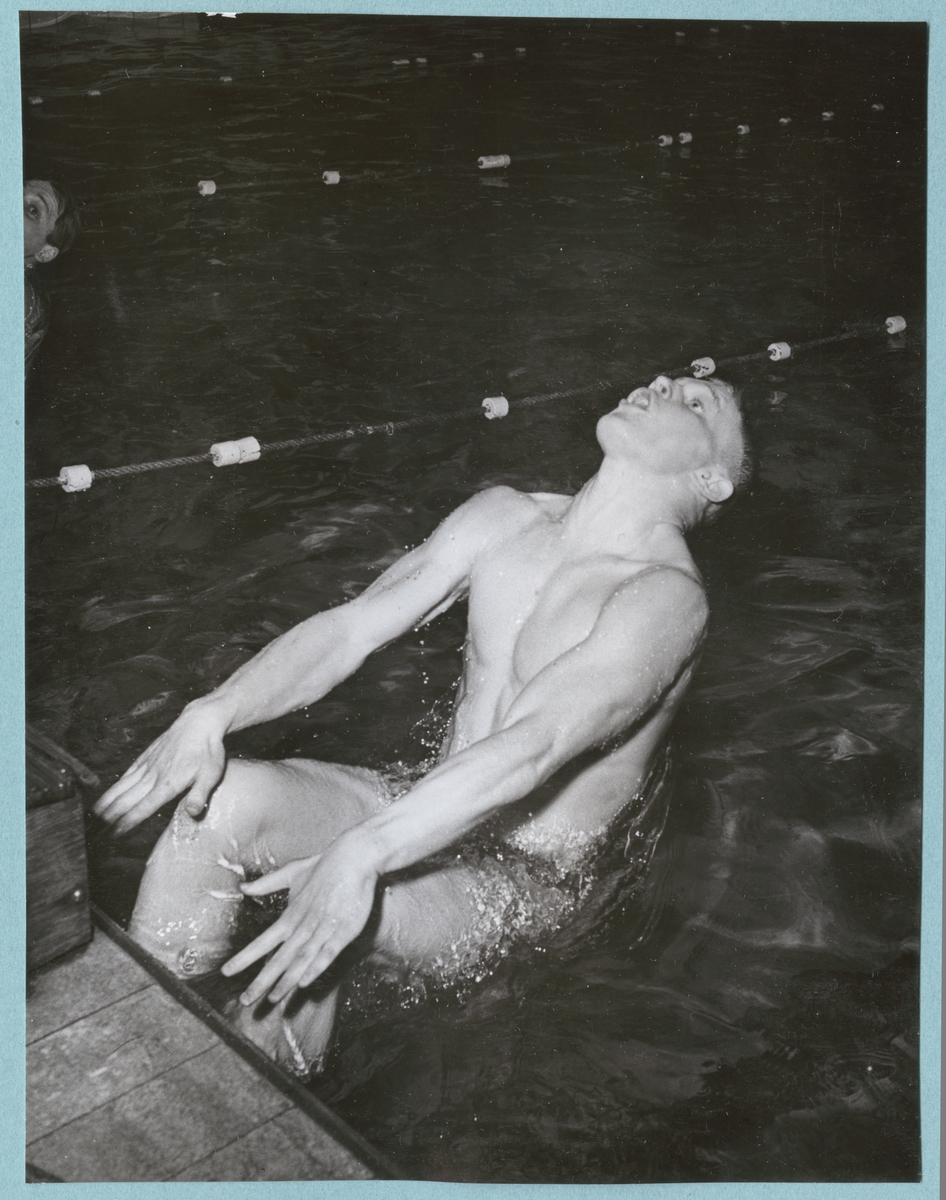 En simmare kastar sig bakåt i vattnet från kanten i en simbassäng. Fotot är daterat till 15-3-52