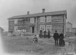 Gruppe foran vinterstua. Hest med slåmaskin. Bak: buret med 