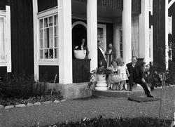 Fire kvinner, en mann og en jentunge foran en villa. Stedet 