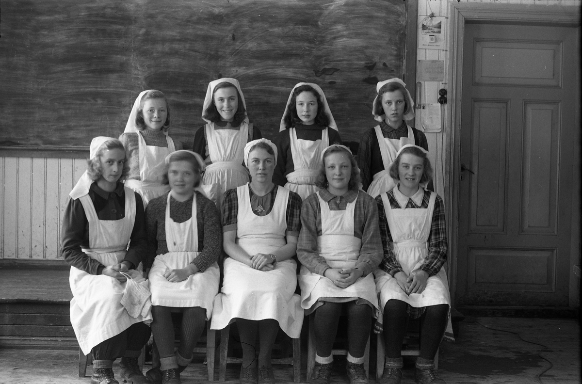 Sju bilder av jenter på "kokkeskole", trolig Hoffsvangen skole 1945. Foran sitter husstellærer Aslaug Glemmestad, senere gift Wedøe. Bak fra venstre (bilde nr. en): Edel Nettum, ukjent, Bjørg Kristiansen, Solveig Jensen, Kari Karsrud, Jorun Tørnby, Petra Stenbak, Jorun Løvstad (?).