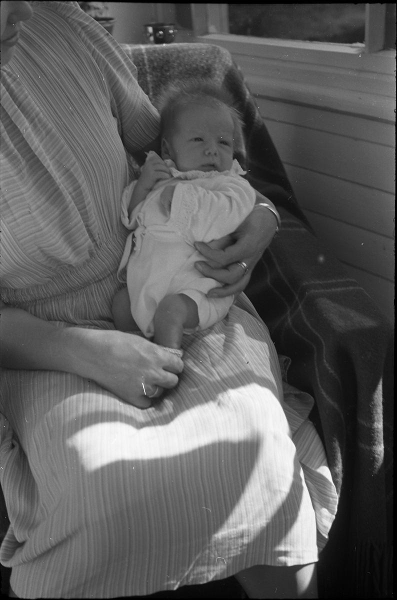 Uidentifisert lite barn. Serie på 10 Bilder. På noen av bildene holdes barnet av kvinner som bare delvis vises, og som heller ikke er identifisert.