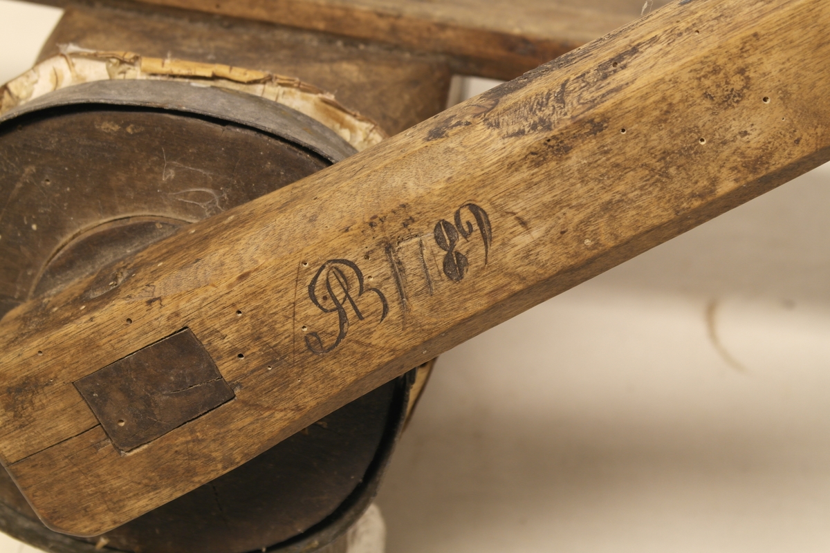 Potetkvern i tre. Kverna er laget av to trestokker som er hulet ut og satt sammen med jernbånd i begge ender. Skrue/Kall inni hulrommet, påmontert ei sveiv på utsiden. Kverna er festet til ei fjøl. Initialer og årstall er inngravert i sveiva.