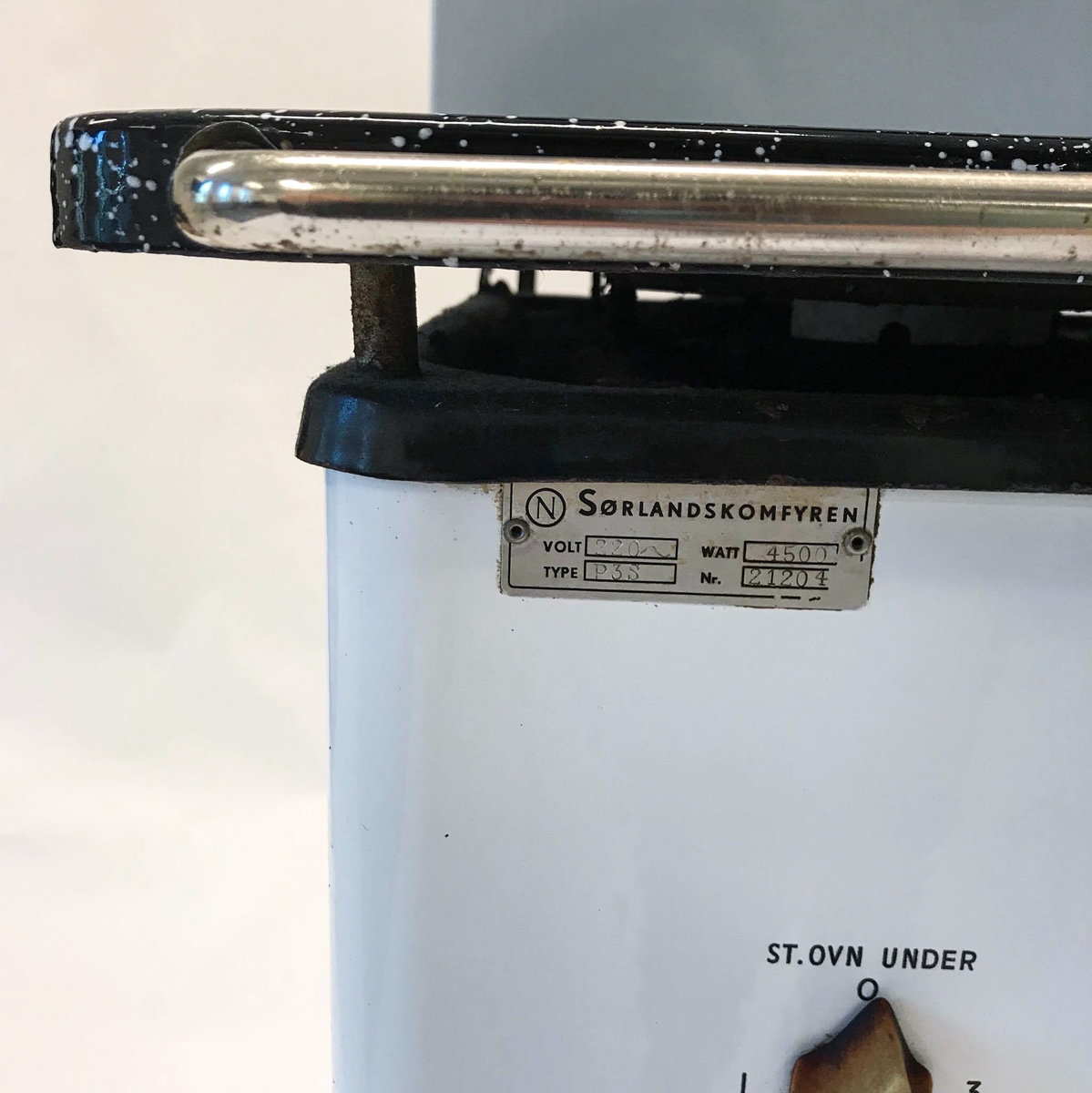 Elektrisk komfyr med bakvegg og tre kokeplater. Stekeovn med termometer på utsiden. I stekeovnen er det to tilhørende stekebrett. Lyspære på bakveggen.