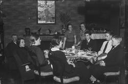 Ungdom og voksne samlet rundt bord i stue.