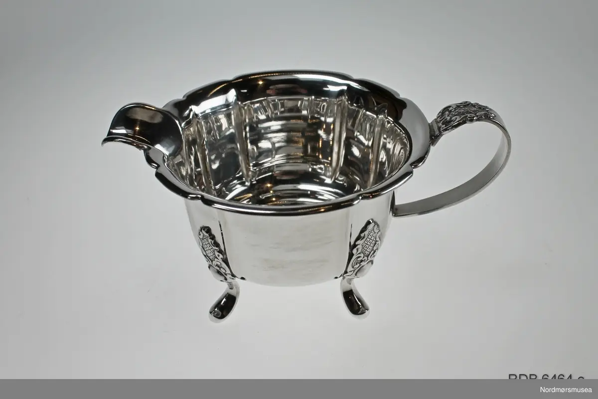 Fløtesett som består av et brett, en sukkerkopp og en fløtemugge i sølvplett. Brettet har innrisset dekor i bunnen. Sukkerkopp og fløtemugge har 4 føttet og hank. Dekor over hver fot og øverst på hanken. En løs papirlapp med påskrift "Raufoss 1952 1. premie 17 km " ligger på brettet.