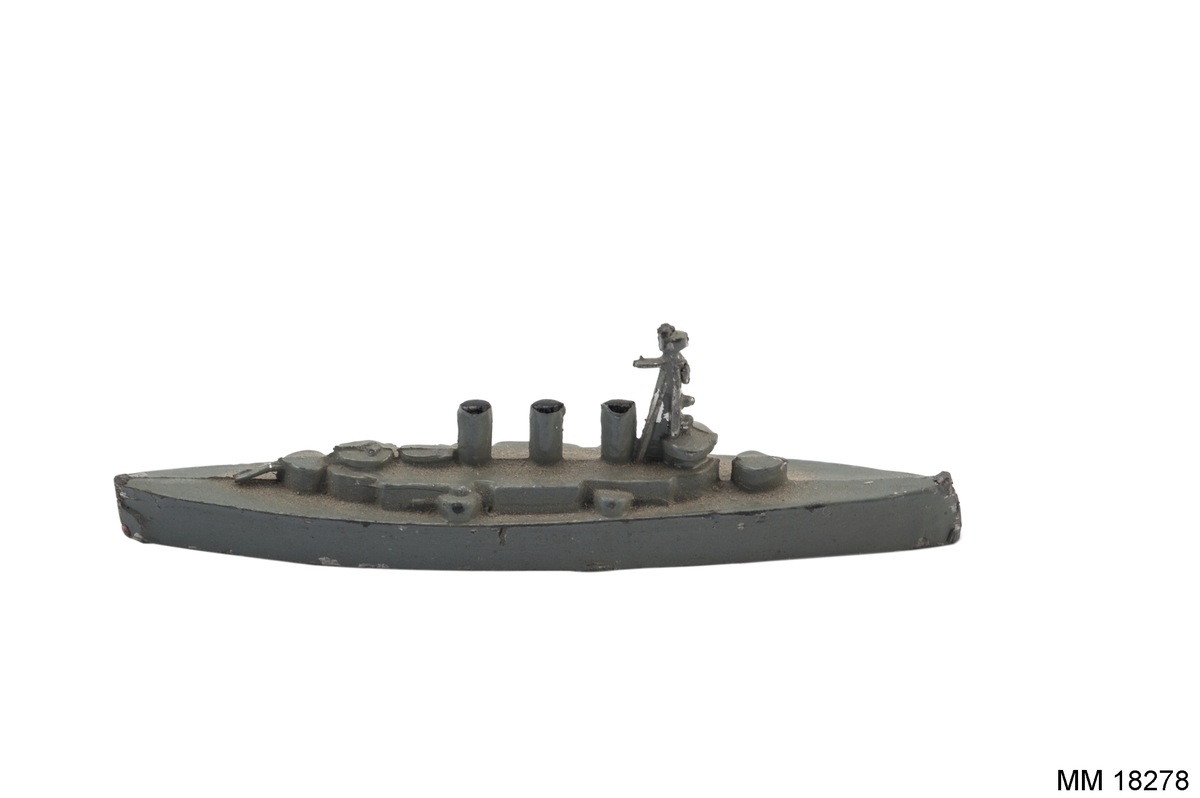 Fartygsmodell i form av pansarskeppet Oscar II gjuten av metall i ett stycke, målad i grått. Spetsig för och akter. Plan botten. Artilleripjäser i för, akter och sidorna. Mast samt tre skorstenar. I botten skrivet fartygets namn.