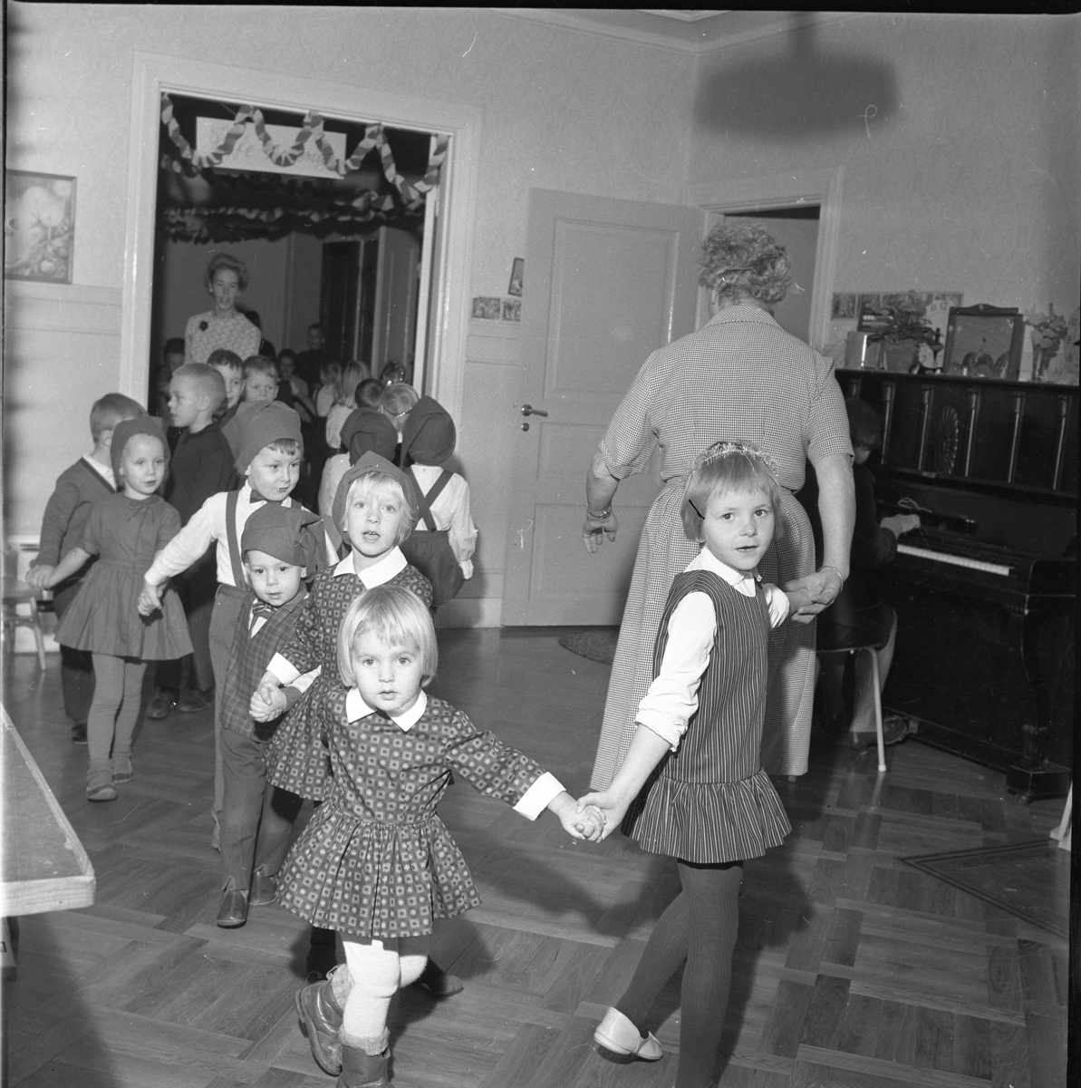 Ringdans på lekskolan i Gränna, jultid 1963. Okända barn i tomteluva leds av Anna-Lisa "Nalle" Lundin.