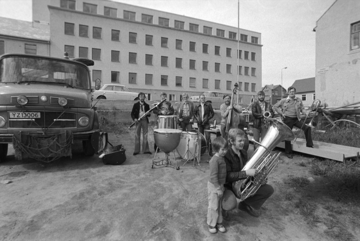 Divisjonsmusikere med instrumenter, fotografert i sivil utendørs med gammelsykehuset i bakgrunnen.