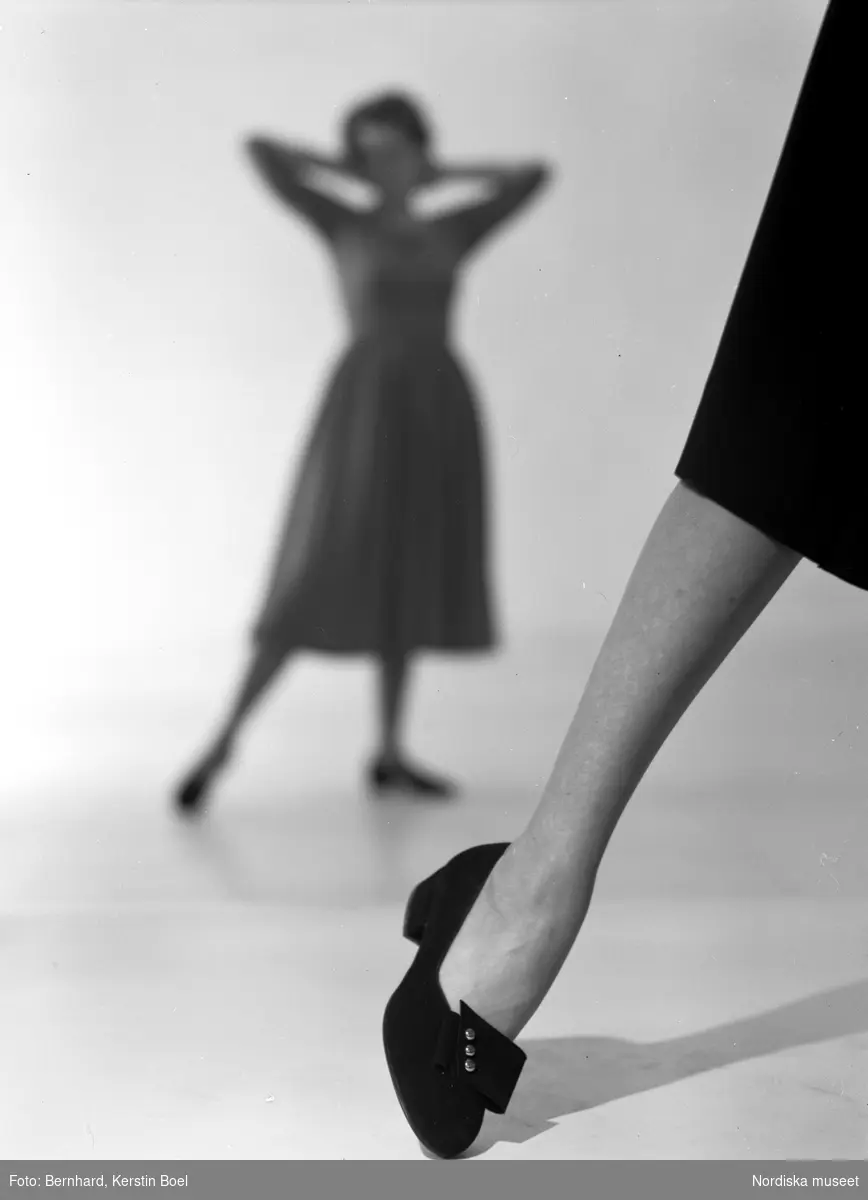 Skomode. I förgrunden en kvinnas ben med klacksko, i bakgrunden poserande modell i klänning.