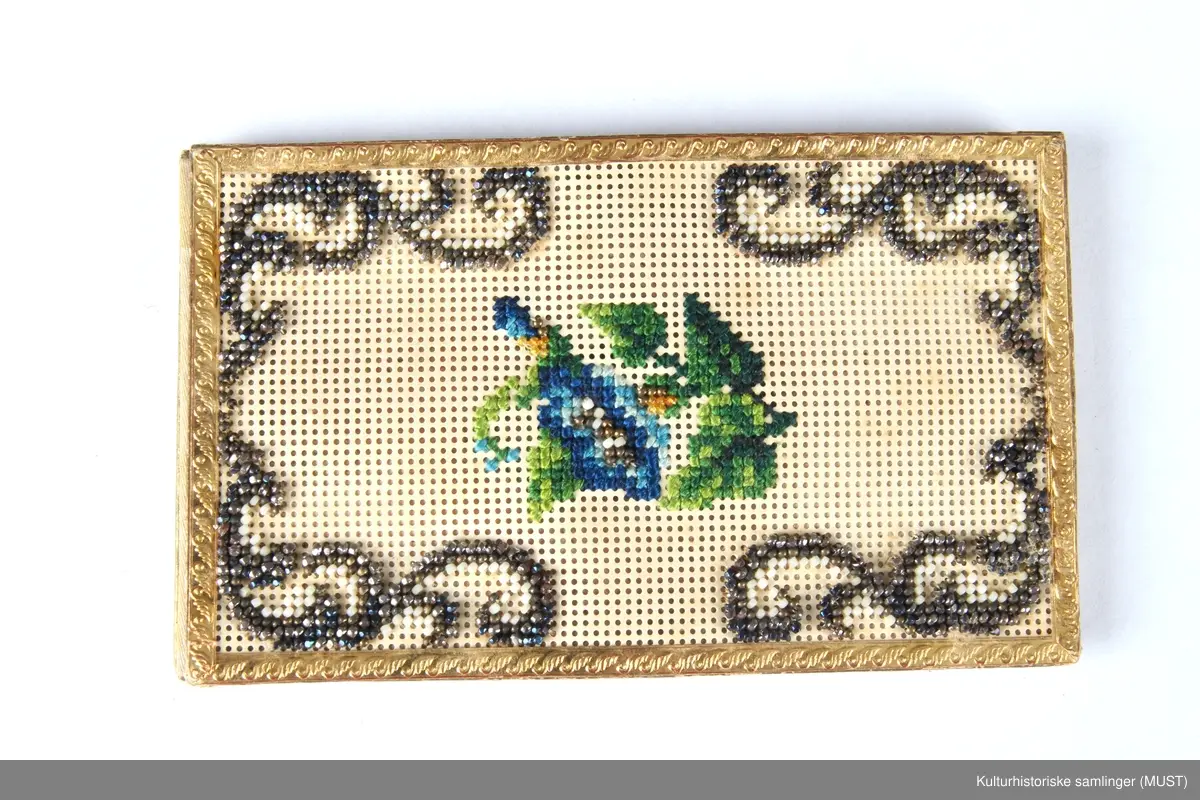 Visittkortmappe av papp. Permene består av hvit, perforert pappkartong og hvit silke. På permene korsstings- og perlebroderier, langs kanten en "gullist".