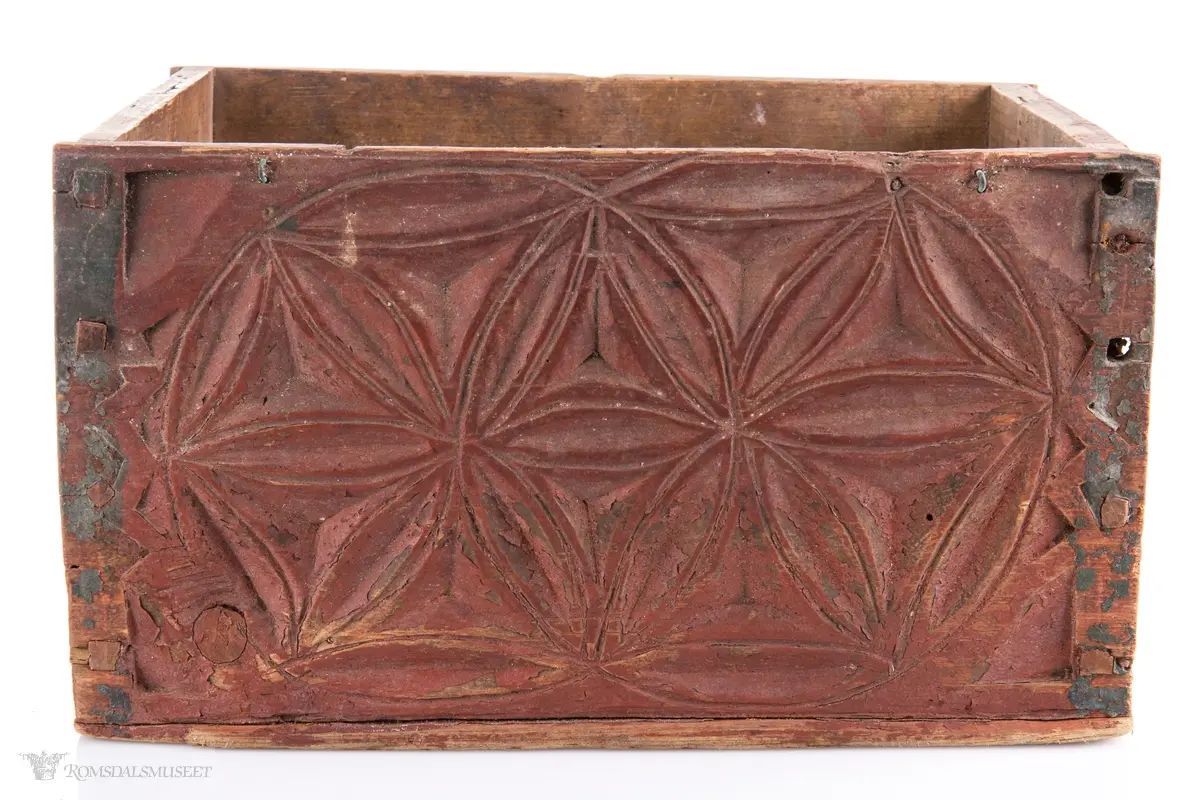 To sammenkomponerte seksbladsrosetter på hver langside. På kortsidene er det skåret ut fire klokkeformede strukturer fylt med spetter og border som til sammen ligner på et noe asymmetrisk solkors/kors.