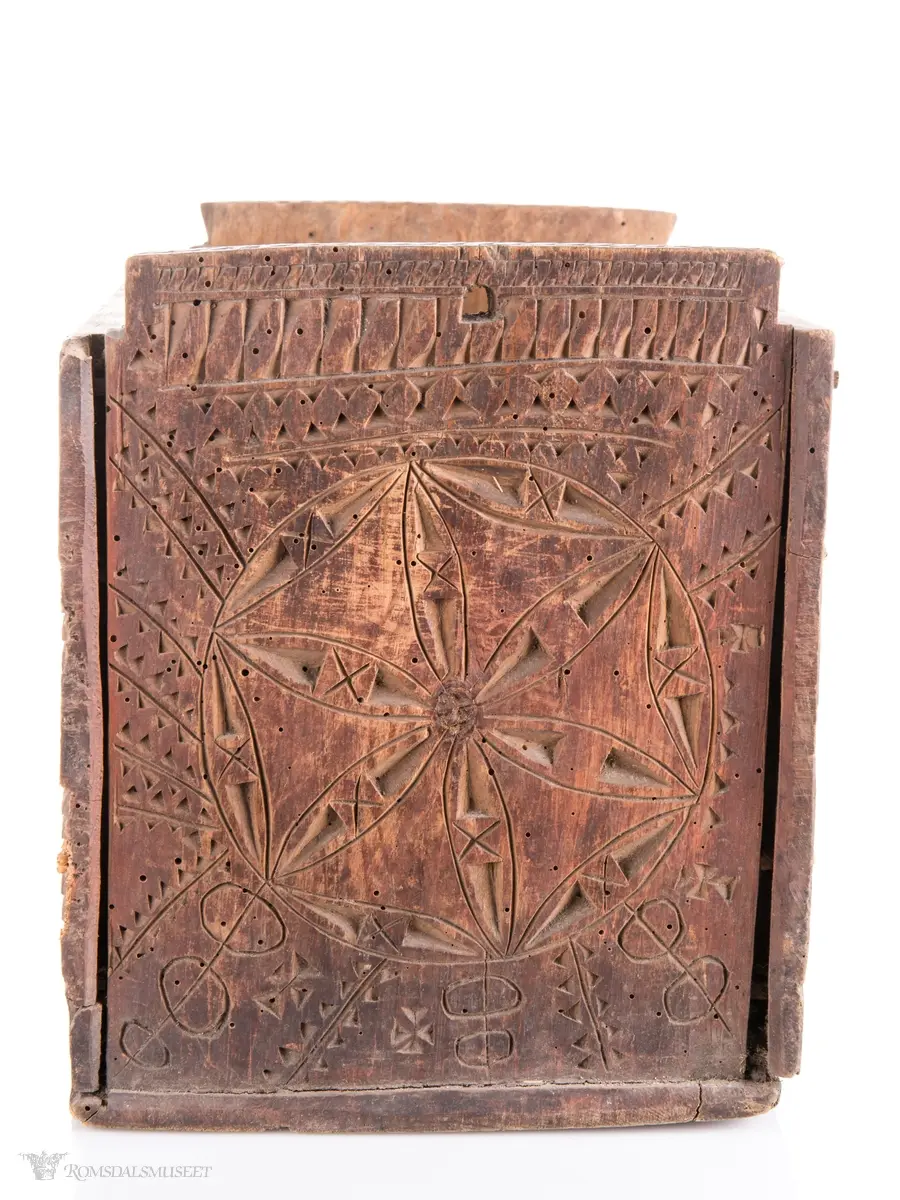 En stor og to små seksbladsroser i karveskurd på langsidene med skraverte dekorfelter og spetter rundt. På kortsidene er det skåret ut en stor seksbladsroser med rike dekorasjonsfelter bestående av spetter, streker diamantformer, sirkler med strek gjennom og solkors/kors. De største rosenen har kryss skåret inn på kronbladene.