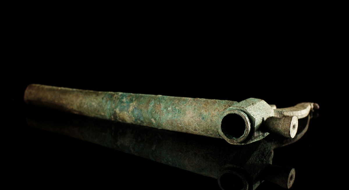 Krantapp av brons inklusive ölhane i kvarsittande i läge. Ölhanen formad som en tupp (stjärten dock ngt ofullständig) Vredhållaren är mångkantig och försedd med ett utsprång.