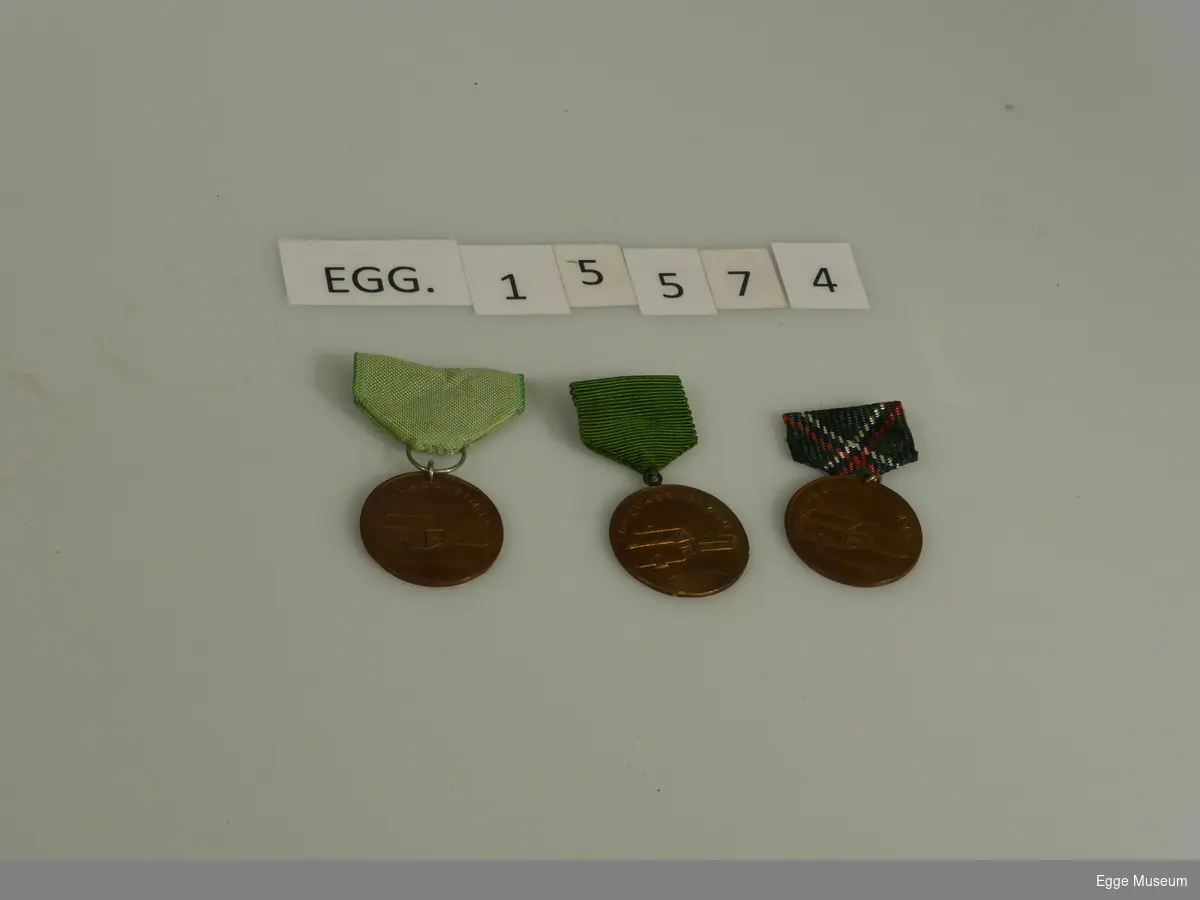 Tre runde medaljer av kobber med ulike bånd. Illustrasjon og tekst på selve medaljen er den samme: "Langvassheimen" og en illustrasjon av husene på Langvassheimen. På baksiden av den ene medaljen er det inngravert "25".

Den ene medaljen har rutete bånd i fargene grønn, rød, svart og hvit. Den andre har lysegrønt bånd og den tredje medaljen har mørkegrønt bånd.