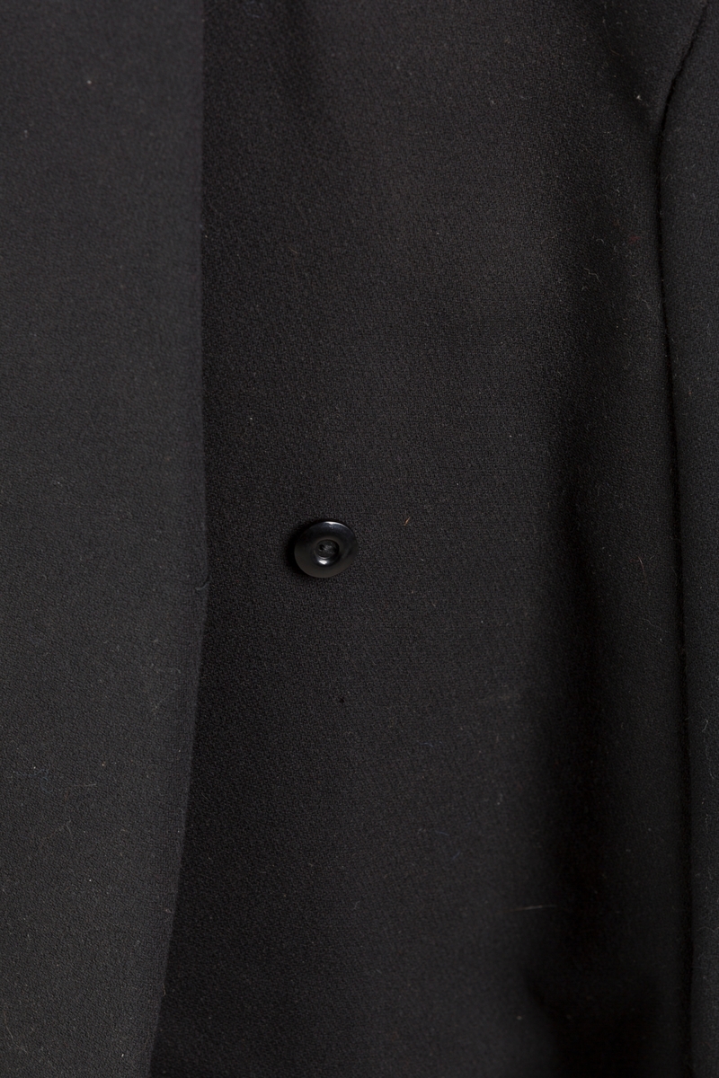 Sort med for i silke på hver side
Tostikklommer, 
Flosset innside
Tre knapper i plast med forskjellig utførelse to store, like, og en mindre.
Bred mansjett med splitt