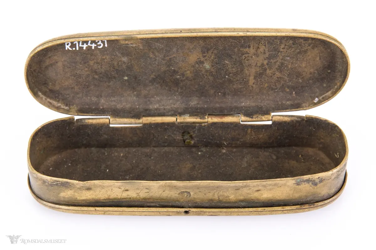 Rektangulær messingeske med avrundede ender. Har en påsatt og påklinket utenpåliggende bunn og utenpåliggende, hengslet lokk