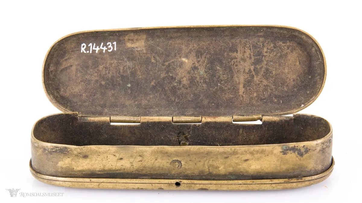 Rektangulær messingeske med avrundede ender. Har en påsatt og påklinket utenpåliggende bunn og utenpåliggende, hengslet lokk