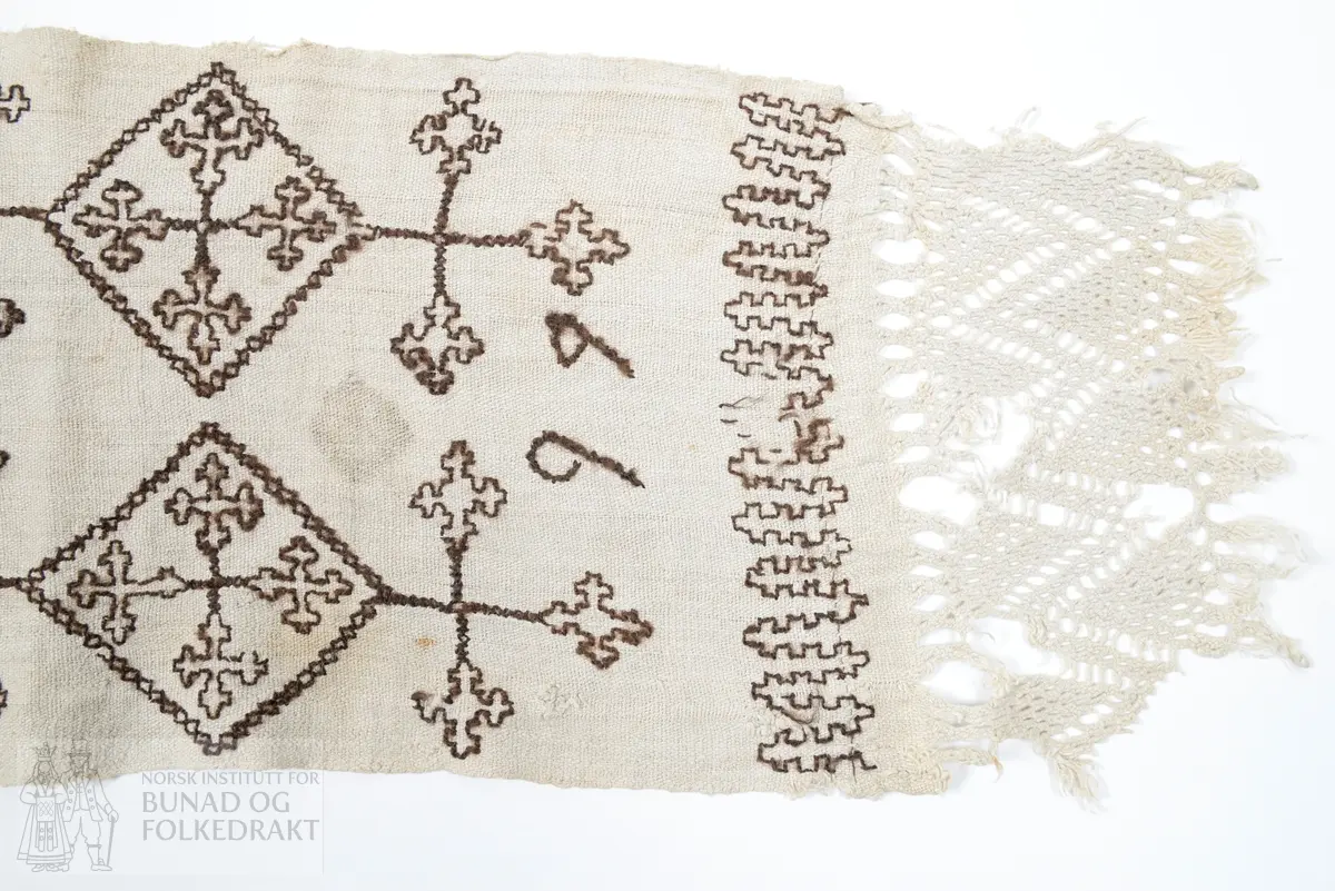 Er usikker på bruken av tekstilen. Kan ha vore sendingsplagg, hovudklut eller bårekross?
Av grov mjuk ubleika linlerret. Jare i båe langsidene. Broderi med holbeinsting med sauebrunt ullgarn. Båe endane har påsydd eit stykkje av liknande linkvalitet, der efsingane er knytt i firflettingsteknikk. Initialane MKD og årstalet 1799.