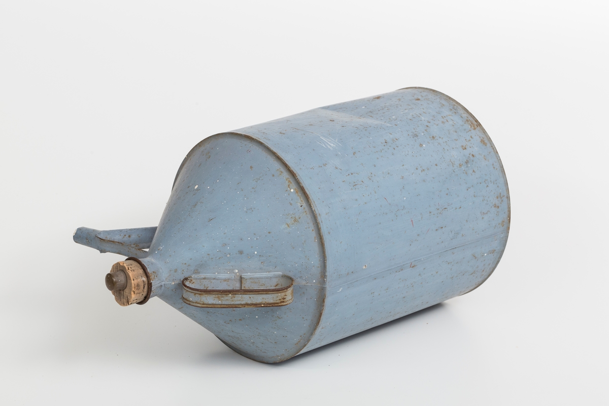 Kanne i sink, blå. Korket i tuten og korklokk med plast. Har håndtak og helletut. Kannen har påklistret god jul merkelapp med navn. Delvis avrevet.