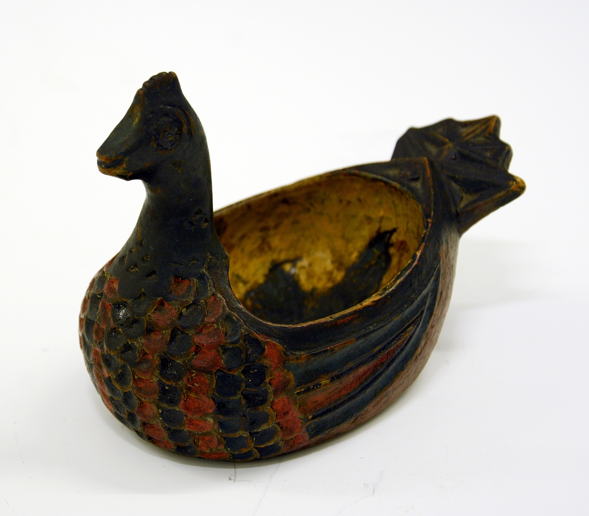 Ølhøne. Fra protokollen: Koks, liten og høneformet, malt. Hovedet kort, med kam, brystet skaaret i fjærskjæl, siderne i vinger, halen kerbsnit. Under skaaret "Birgiet 1774". Malt i rødt og blaagrønt, gult indeni.