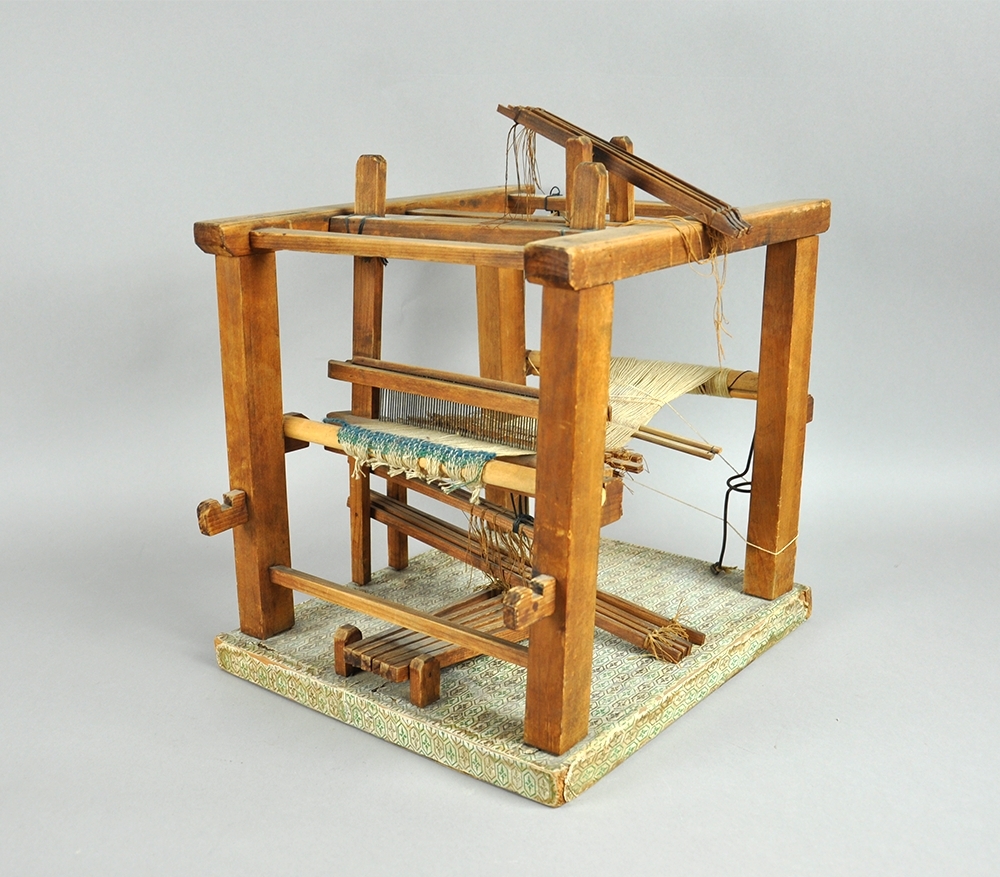 Liten modell av en flatvev med renning, vevskje, garnbom, slagbom, brystbom og trøer.